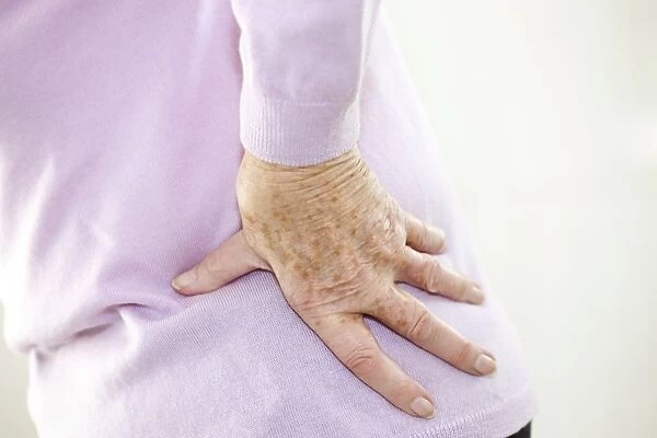 Back pain. MODEL RELEASED. Back pain. Elderly woman holding her painful back