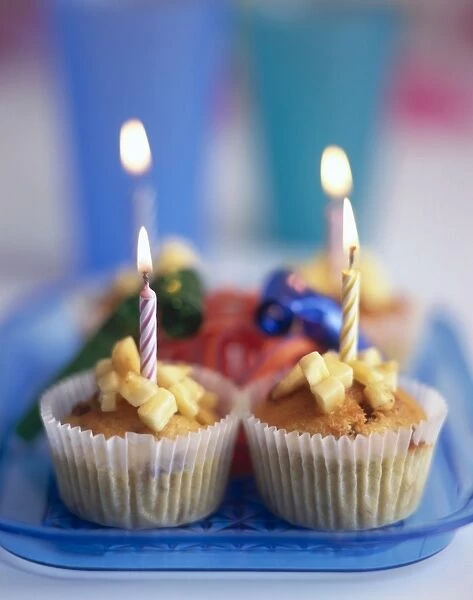 Two fruity birthday fairy cakes with lighted candles in them