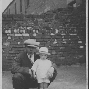 A father poses with his little boy in a back street. Date: 1920s