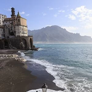 Fancy street lamp, rusty anchor and wave breaking on beach, distant church, Atrani