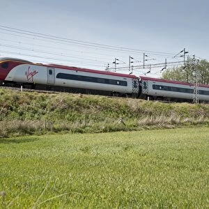 Virgin railway train travelling along bank in farmland, Wrinehill, Staffordshire, England, may