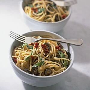 Bowls of spaghetti with olives, sun-dried tomatoes and basil, forks on top