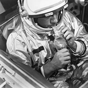A NASA test subject consumes a meal of pot roast and gravy through a feeding tube pack aboard a Gemini spacecraft mockup
