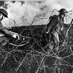 British troops advancing through barbed wire during a training drill. September 1943