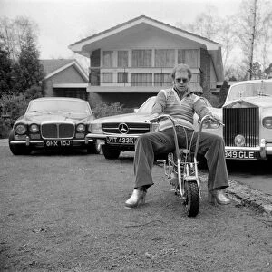Elton John pictured at his home, sitting on a small motorbike in front of four of his